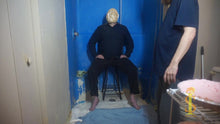 Man sitting on stool has pie pushed into face. Crust is cracking revealing the cream inside the pie