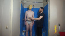Two men. One wearing only briefs, the other wearing all black. The man in briefs has a pie pushed in his face, the crust sticks. The man in black looks at the man with pie in his face