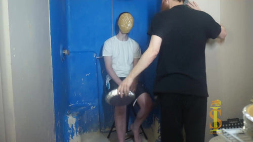 two men, one sitting on stool in white shirt and black shorts. Has pie pushed into face, crust sticking to his face. Second man in wearing all black holds the empty pie tin