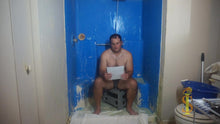 Man sitting on a small stool in a bathroom holding a piece of paper.